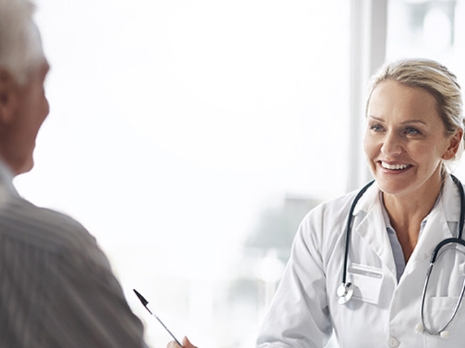 Kvinnelig allmennlege som smiler til pasient.