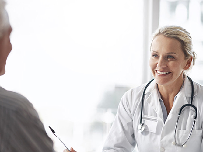 Kvinnelig allmennlege som smiler til pasient.