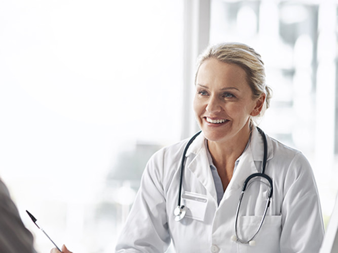 Kvinnelig allmennlege som smiler til pasient.