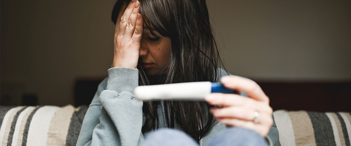 trist kvinne med graviditetstest i sofaen.