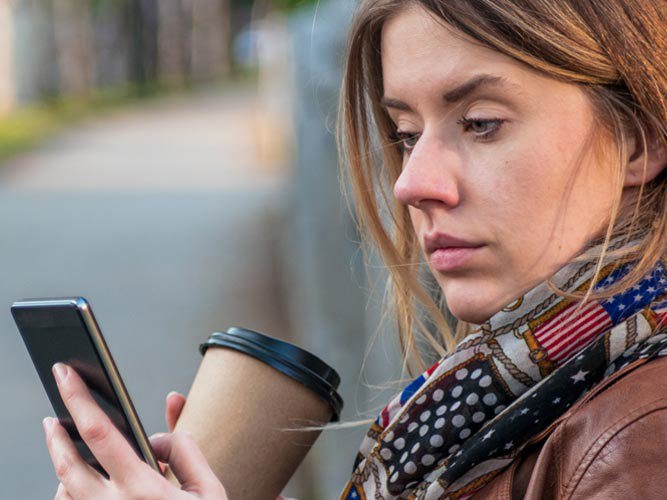 Dame i brun skinnjakke som ser på mobilen.