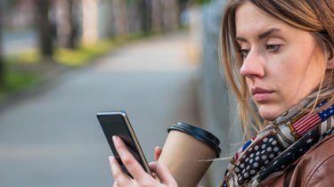 Dame i brun skinnjakke som ser på mobilen.