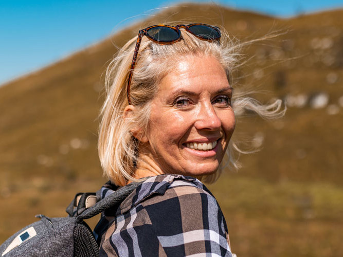 Dame på tur i fjellet som smiler mot kamera.
