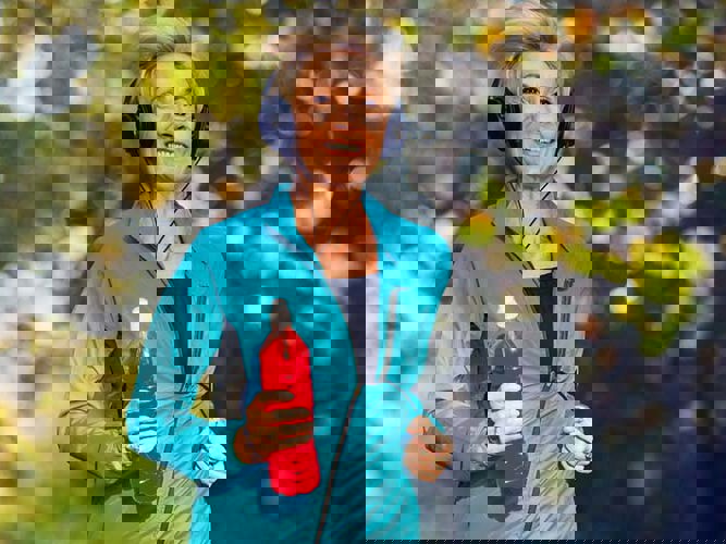 Middelaldrende kvinne jogger fornøyd med en drikkeflaske i hånden. høstlig bakgrunn.