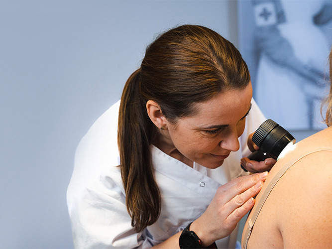 Hudlege sjekker en føflekk på pasient