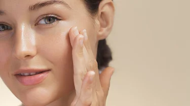 Ung kvinne med vakker hud påfører hudprodukt.