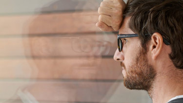 bekymret mann lener seg mot vindu.