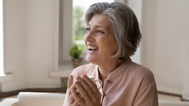 fornøyd dame 60 år sitter i sofaen.